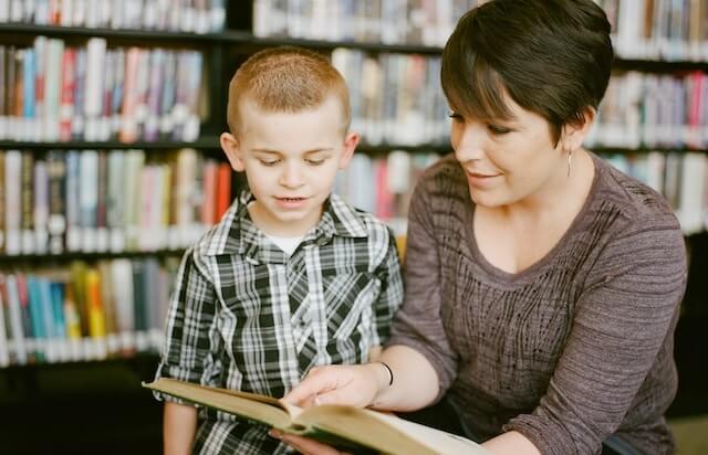 Educator teaching a young boy using a book in a library.