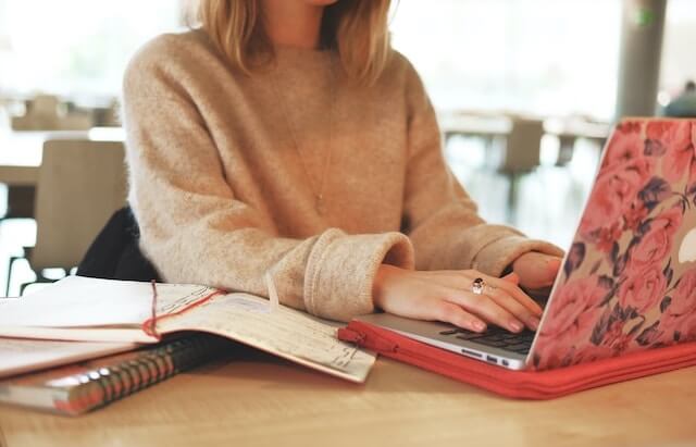 Woman with blonde hair and a comfortable woollen jumper sits at her laptop